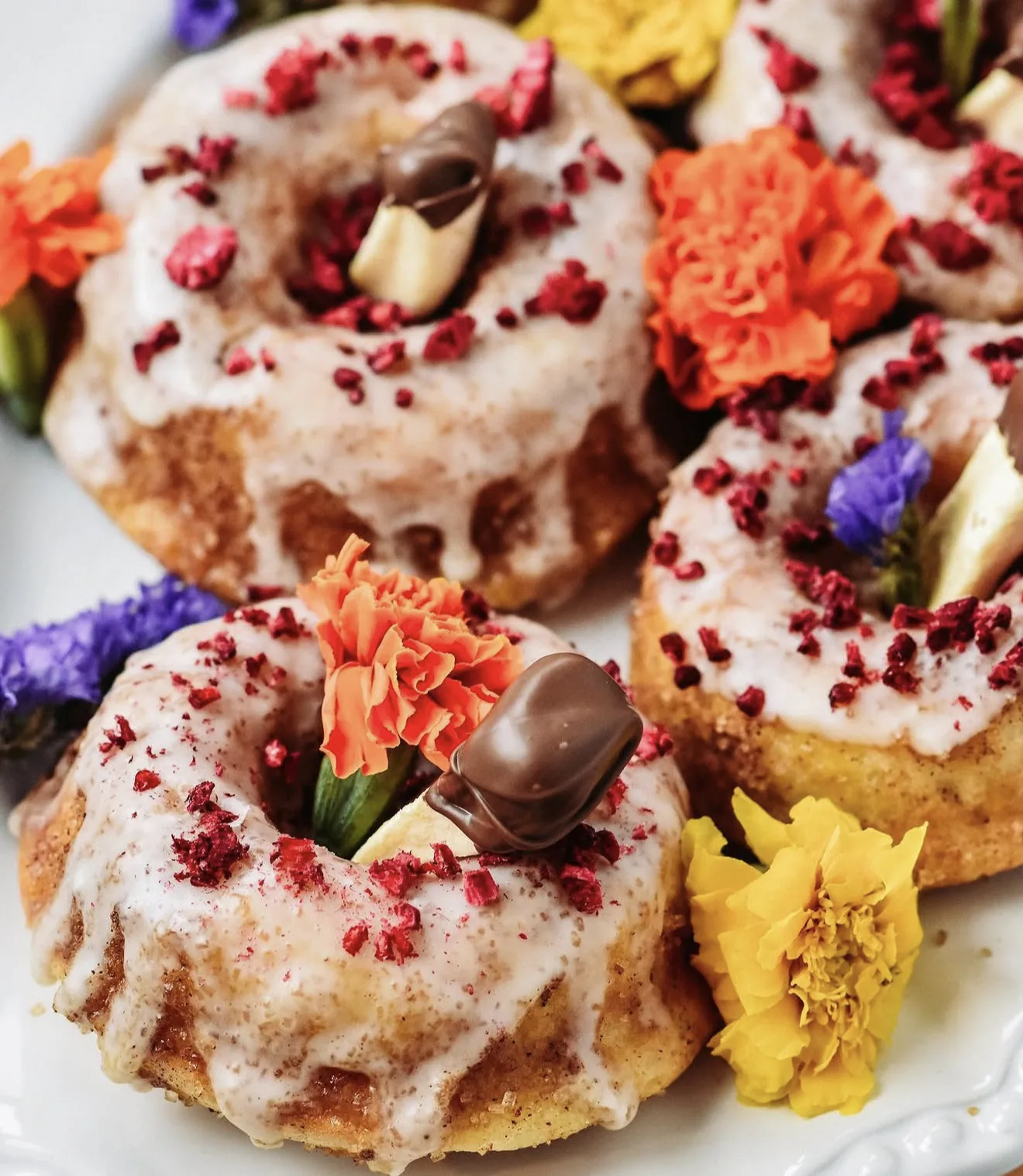 Raspberry crumble lemon donuts on dotted white plate against marble with marigolds and purple blooms