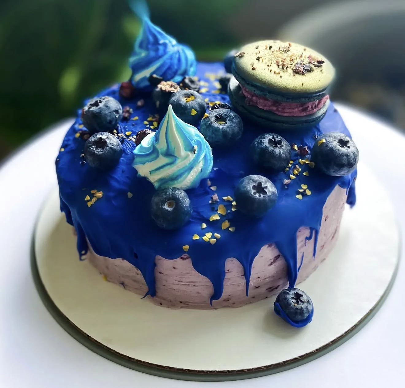 Three royal blue drip mini cakes with macaron toppers meringue kisses and fresh blueberries