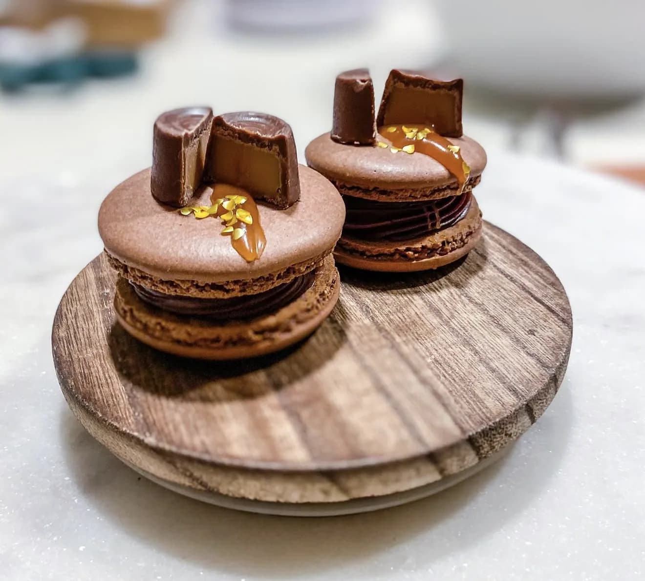 Pink raspberry macarons with chocolate ganache filling and chocolate drip on rustic wood slab