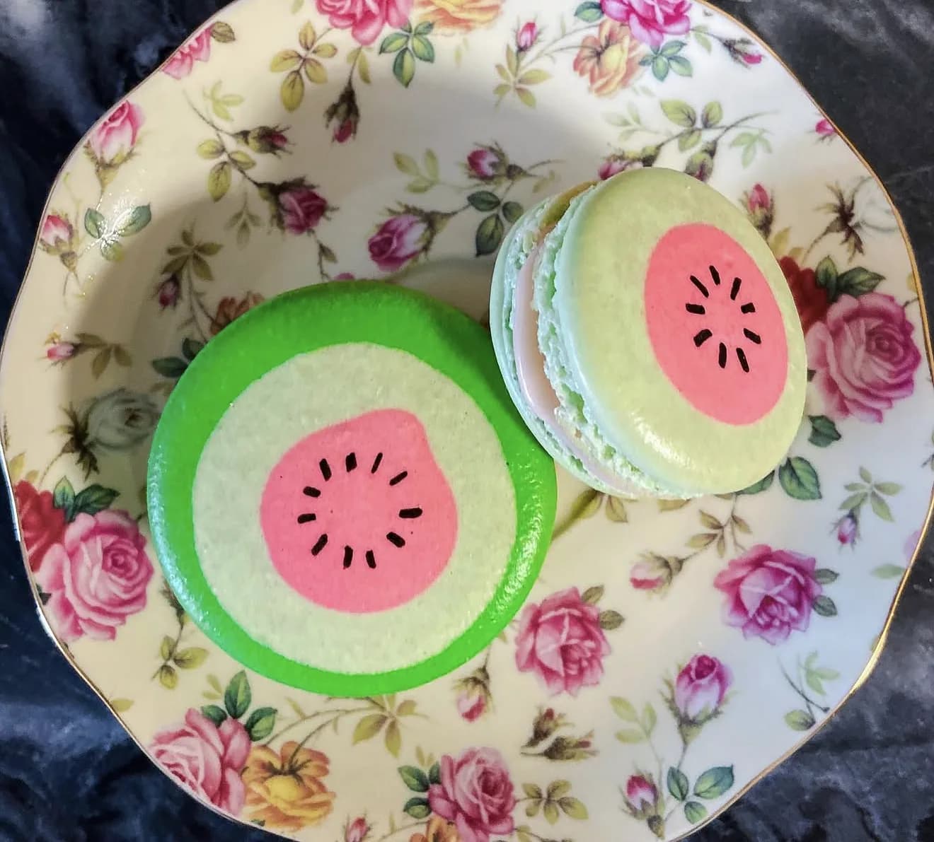 Close duo of green watermelon macaron and pistachio macaron on vintage rose plate